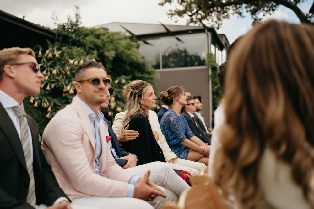 Wedding guests seated in rows of wooden chairs at an outdoor ceremony venue.
