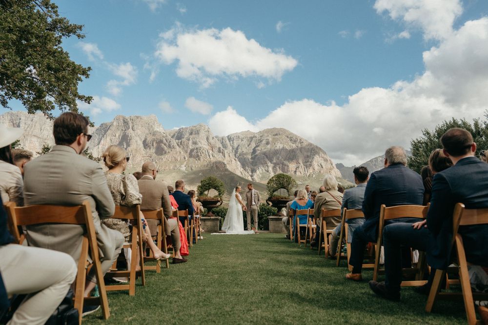 Outdoor wedding ceremony with wooden chairs and dramatic mountain landscape in the background.