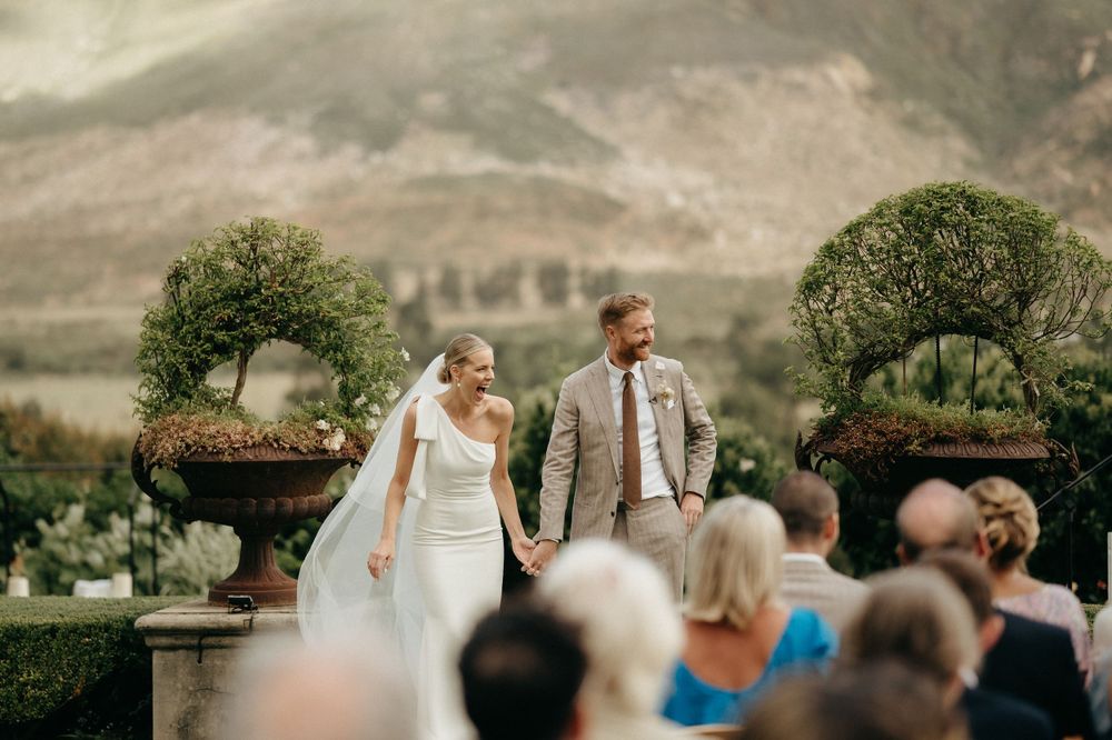 Couple holds hands during their mountain wedding ceremony while guests look on.