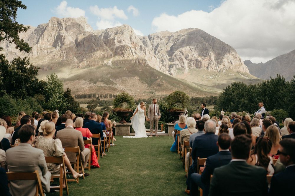 Wedding guests seated on wooden chairs with dramatic mountain peaks rising in the background.
