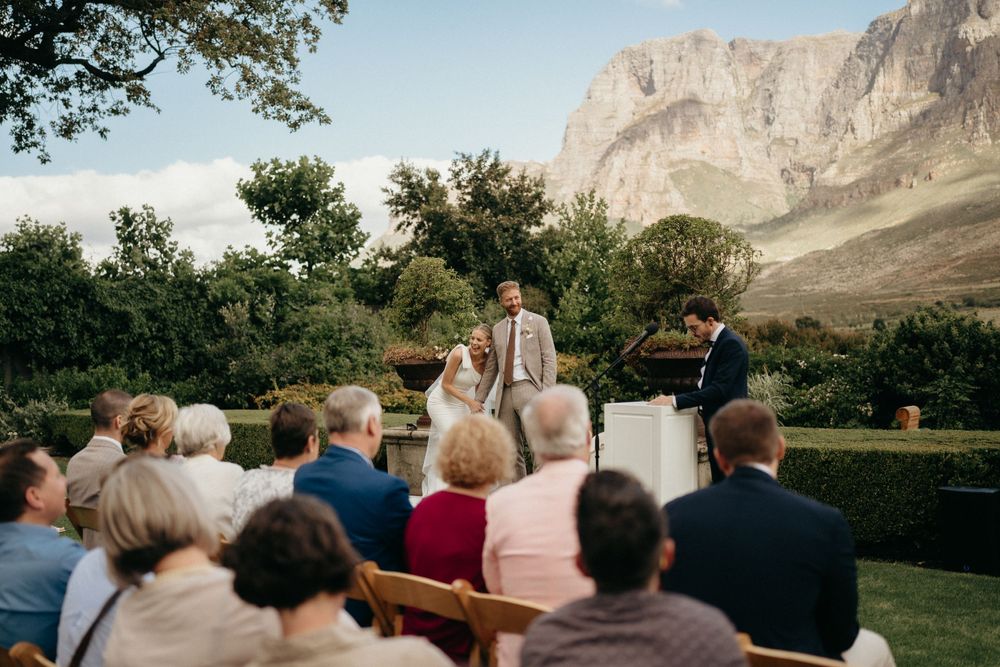 Wedding guests seated on wooden chairs at outdoor ceremony with dramatic mountain backdrop.