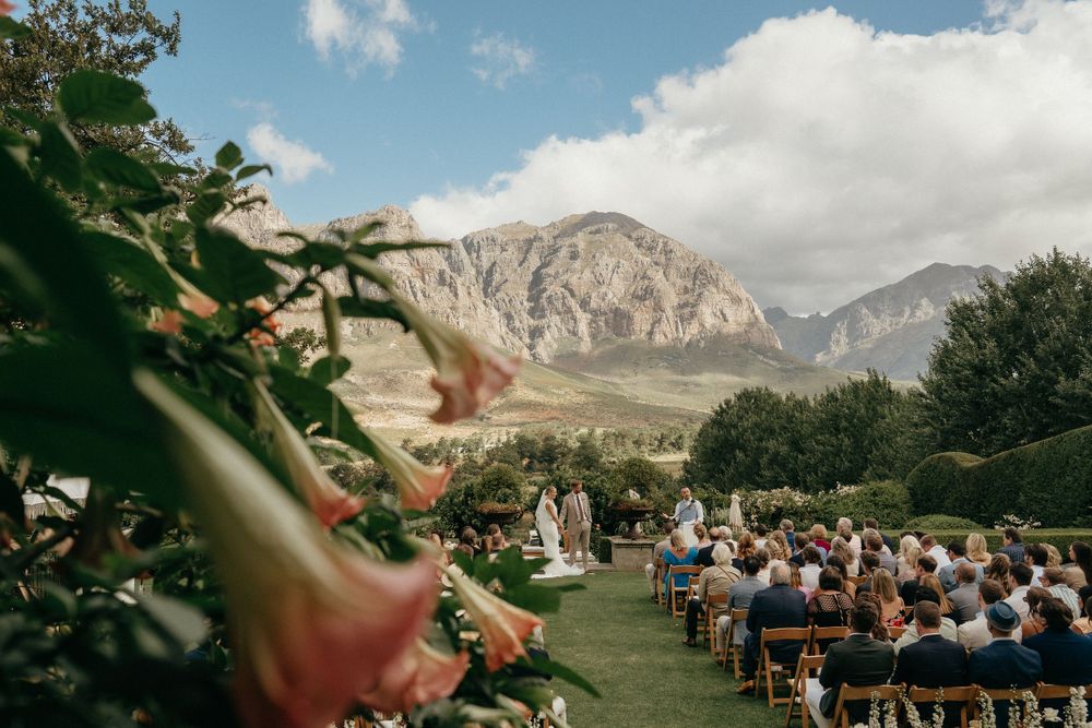 Outdoor wedding venue with dramatic mountain landscape and guests seated on wooden chairs.