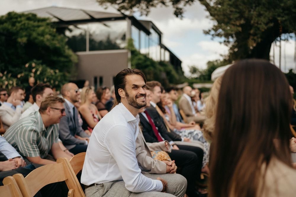 Wedding guests seated in wooden chairs enjoy the outdoor ceremony.