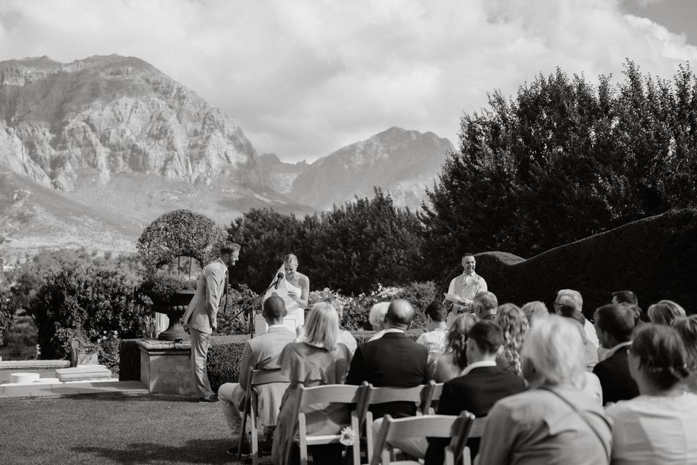 Black and white photo of outdoor wedding ceremony with mountain vista and seated guests.