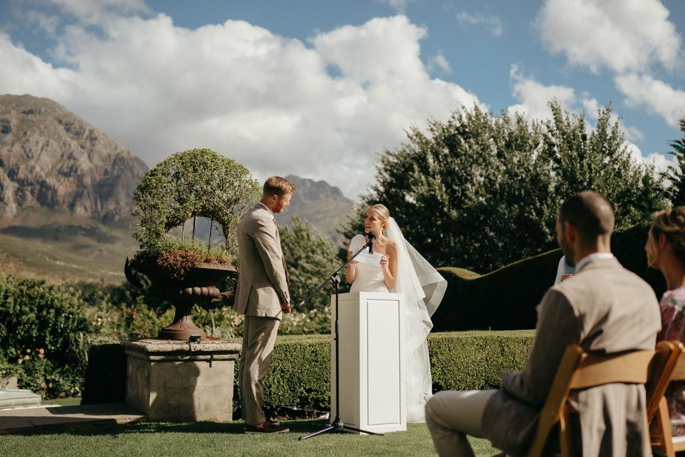 Outdoor garden wedding ceremony with mountain backdrop and decorative potted plants.