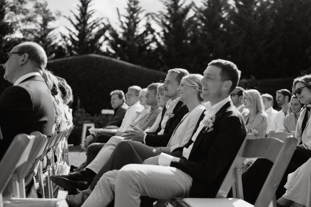 Black and white photo of wedding guests seated in rows of chairs during outdoor ceremony.
