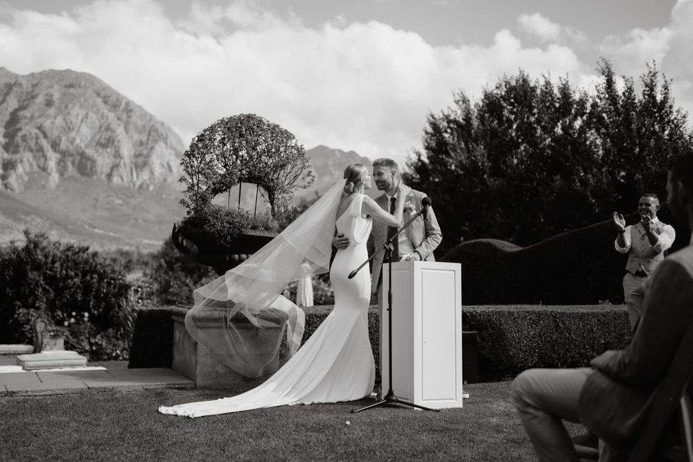 Black and white photo of couple during wedding ceremony with mountains visible in background.