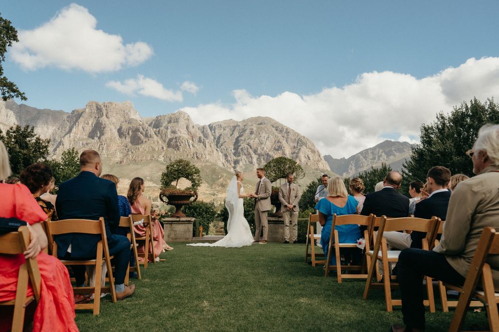 An outdoor wedding ceremony set against dramatic mountain peaks with wooden chairs and natural landscape.