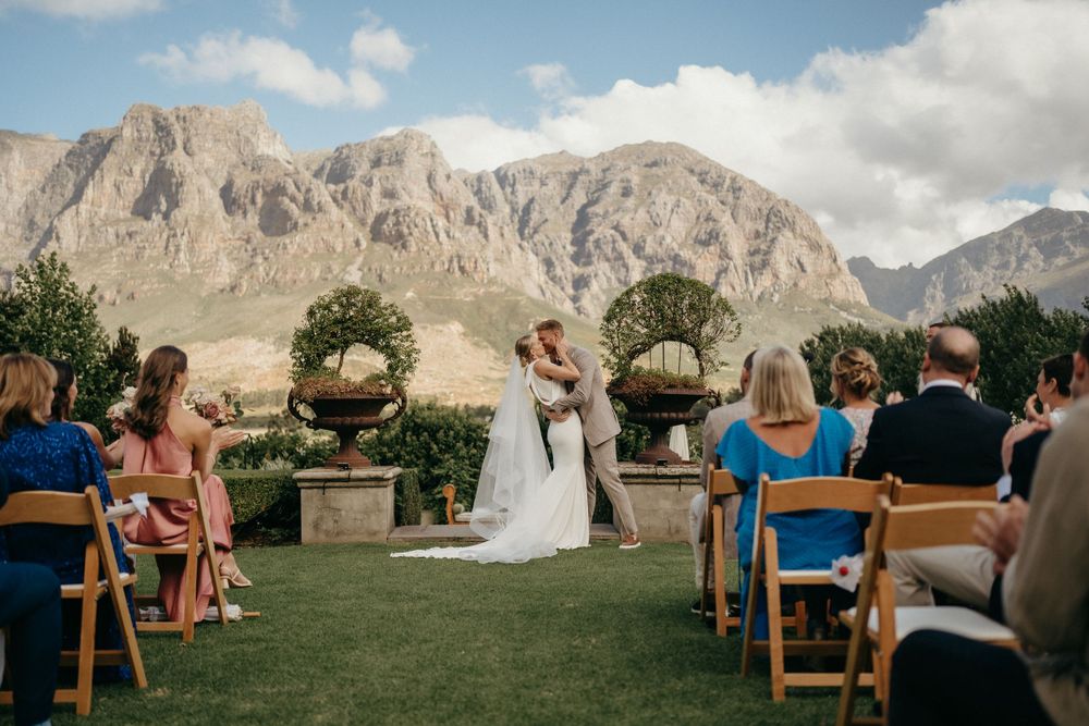 A wedding ceremony setup on a lawn with wooden chairs and majestic mountain peaks in the background.