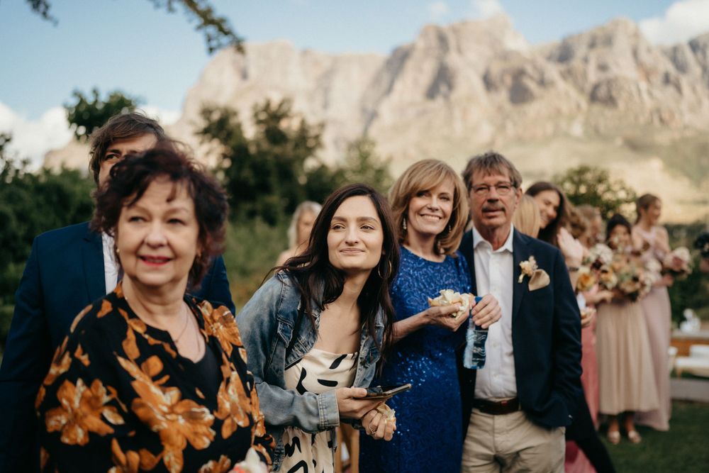 Wedding guests celebrating and smiling outdoors with dramatic mountain peaks in the background.