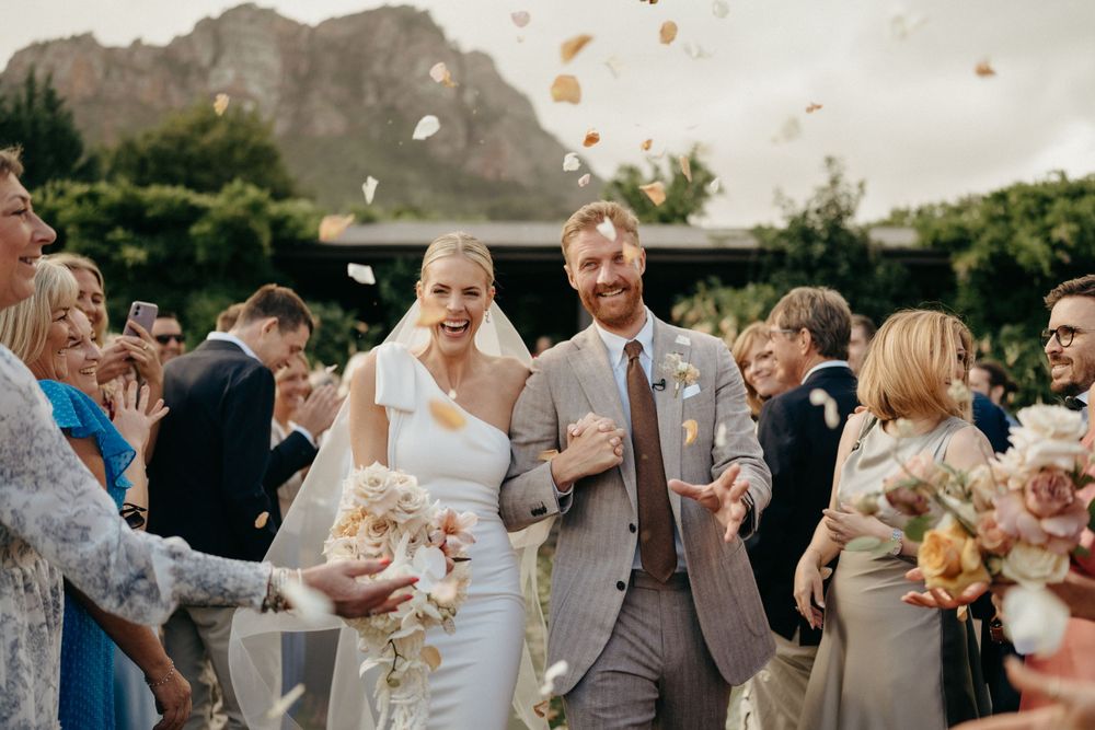 Wedding celebration outdoors with guests throwing confetti near a mountain backdrop.