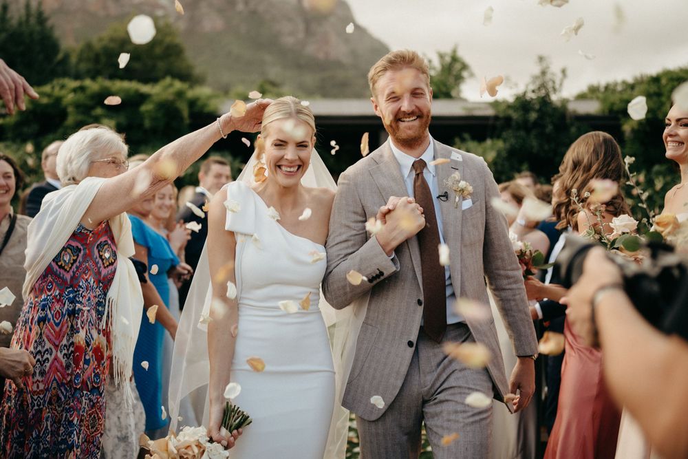 Wedding celebration with guests throwing confetti during outdoor ceremony.
