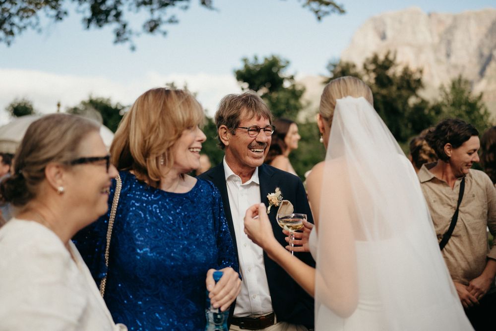 Wedding guests share laughs during outdoor reception with mountain backdrop.