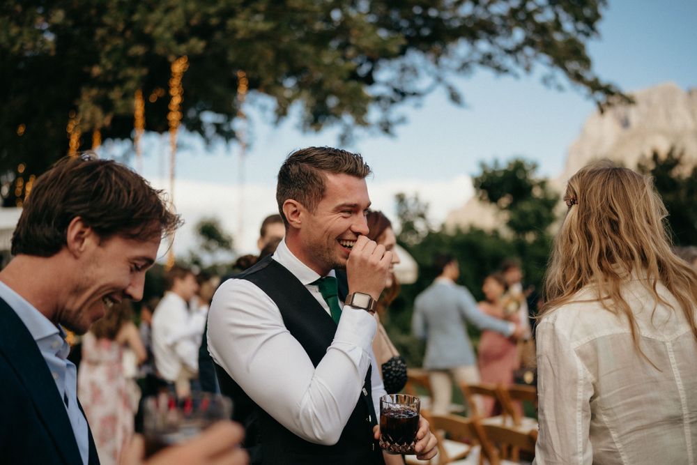 Outdoor wedding reception guests enjoying drinks and conversation at sunset.