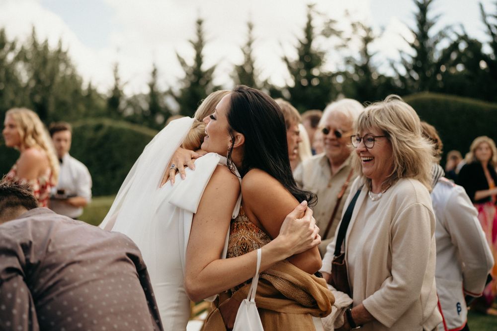 Wedding guests gathered outdoors near evergreen trees sharing joyful moments at a celebration.