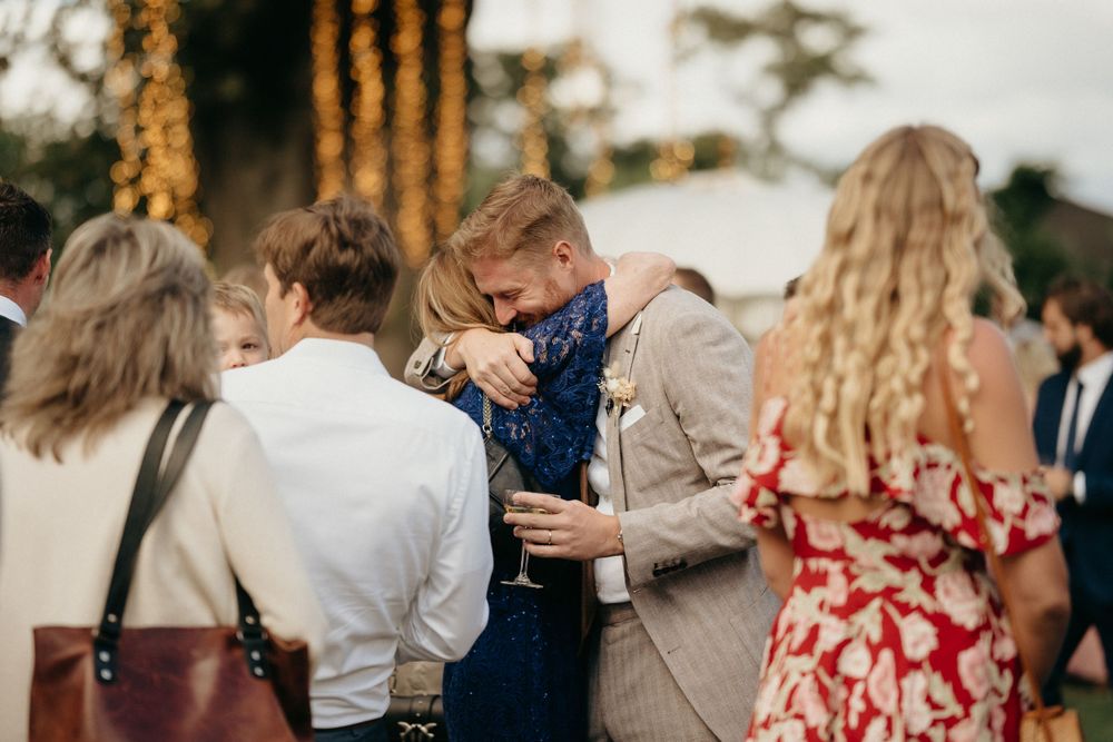 Wedding guests mingle during an outdoor reception with string lights visible in the background.