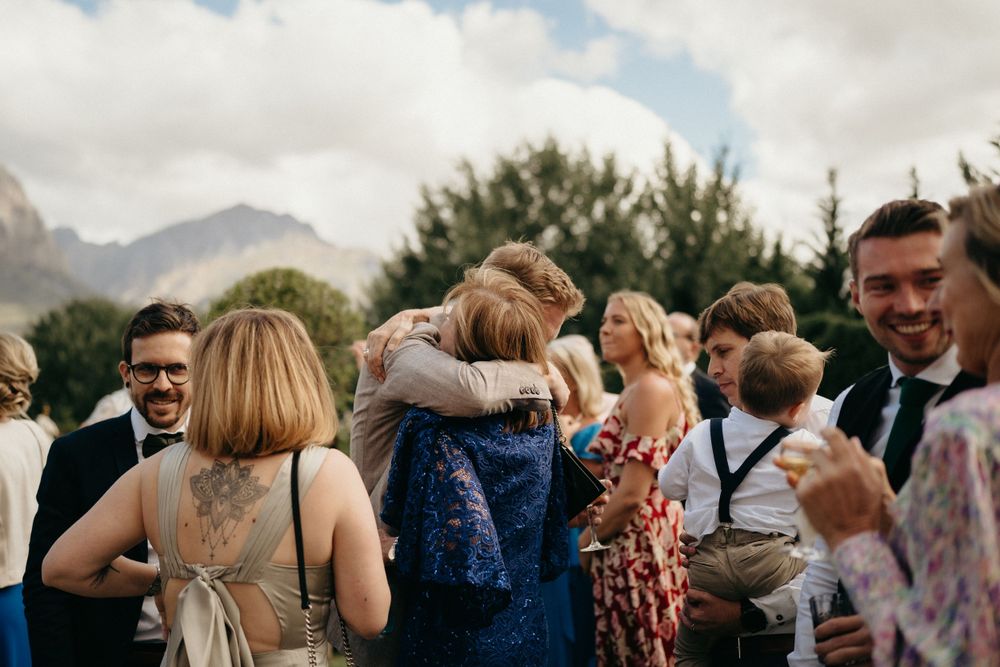 A joyous group embraces at an outdoor wedding celebration with mountains visible in the background.