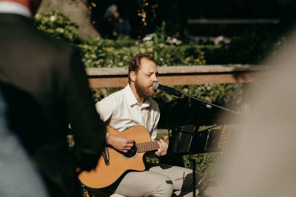 Musician playing acoustic guitar outdoors during a summer gathering.