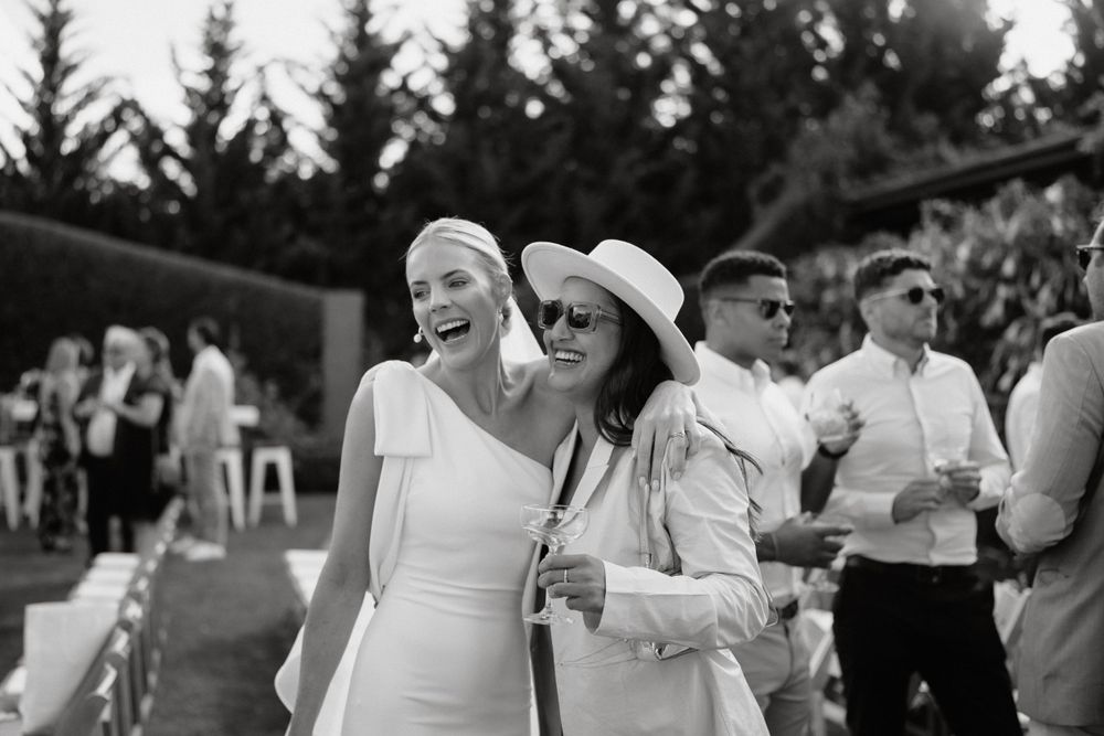 Wedding guests share joyful moments during an outdoor celebration with trees in the background.