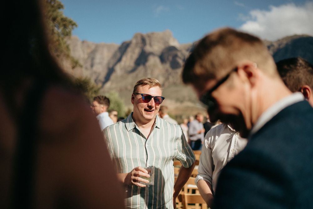 Guests socialize at an outdoor wedding reception with mountain scenery in the background.
