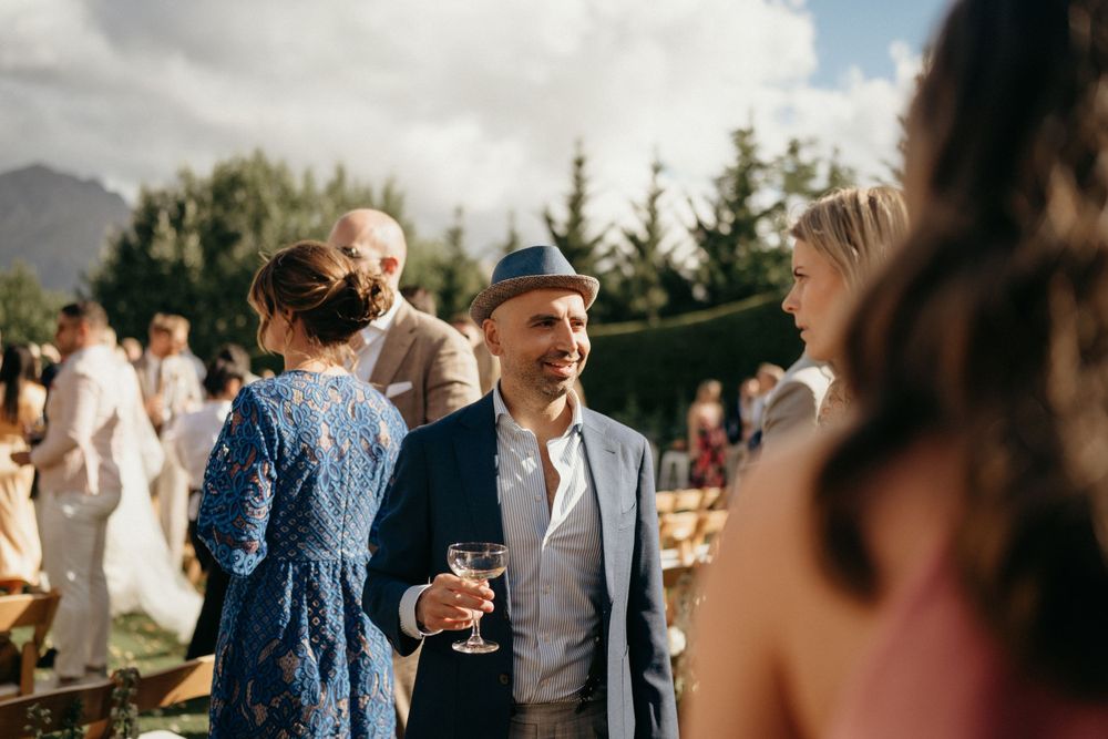 Wedding guests mingling and chatting during an outdoor reception with mountains in the background.
