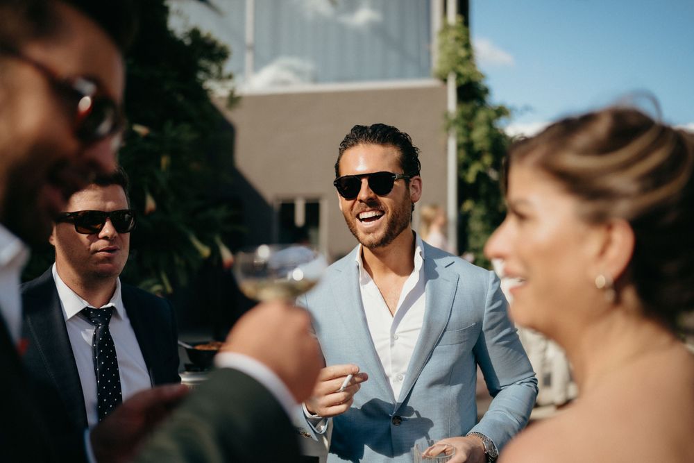 Wedding guests mingling and laughing during an outdoor reception on a sunny day.