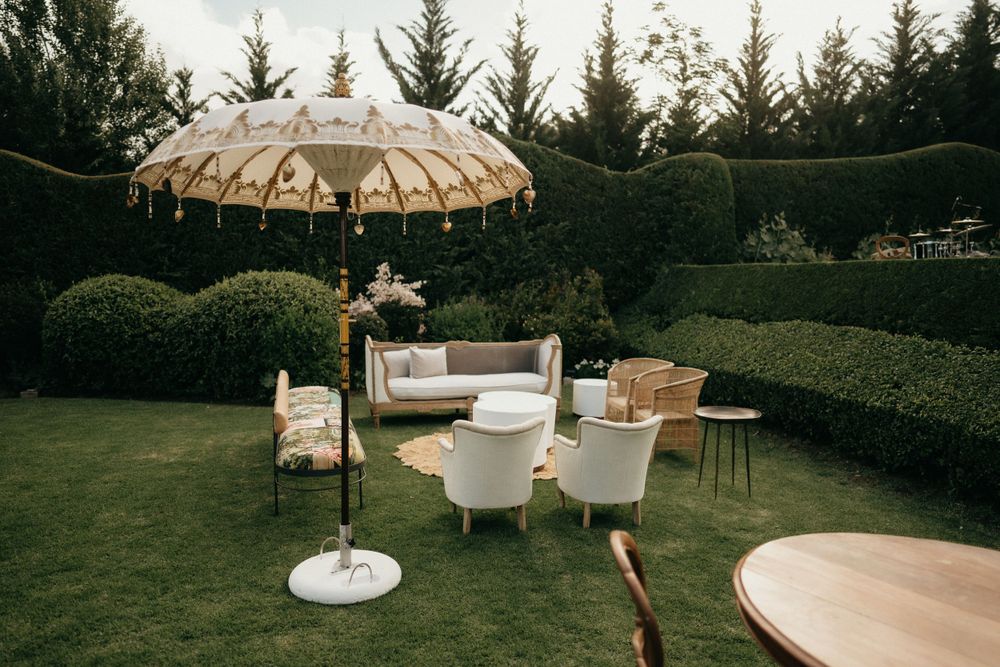 Elegant outdoor garden seating area with white chairs and decorative umbrella shade.