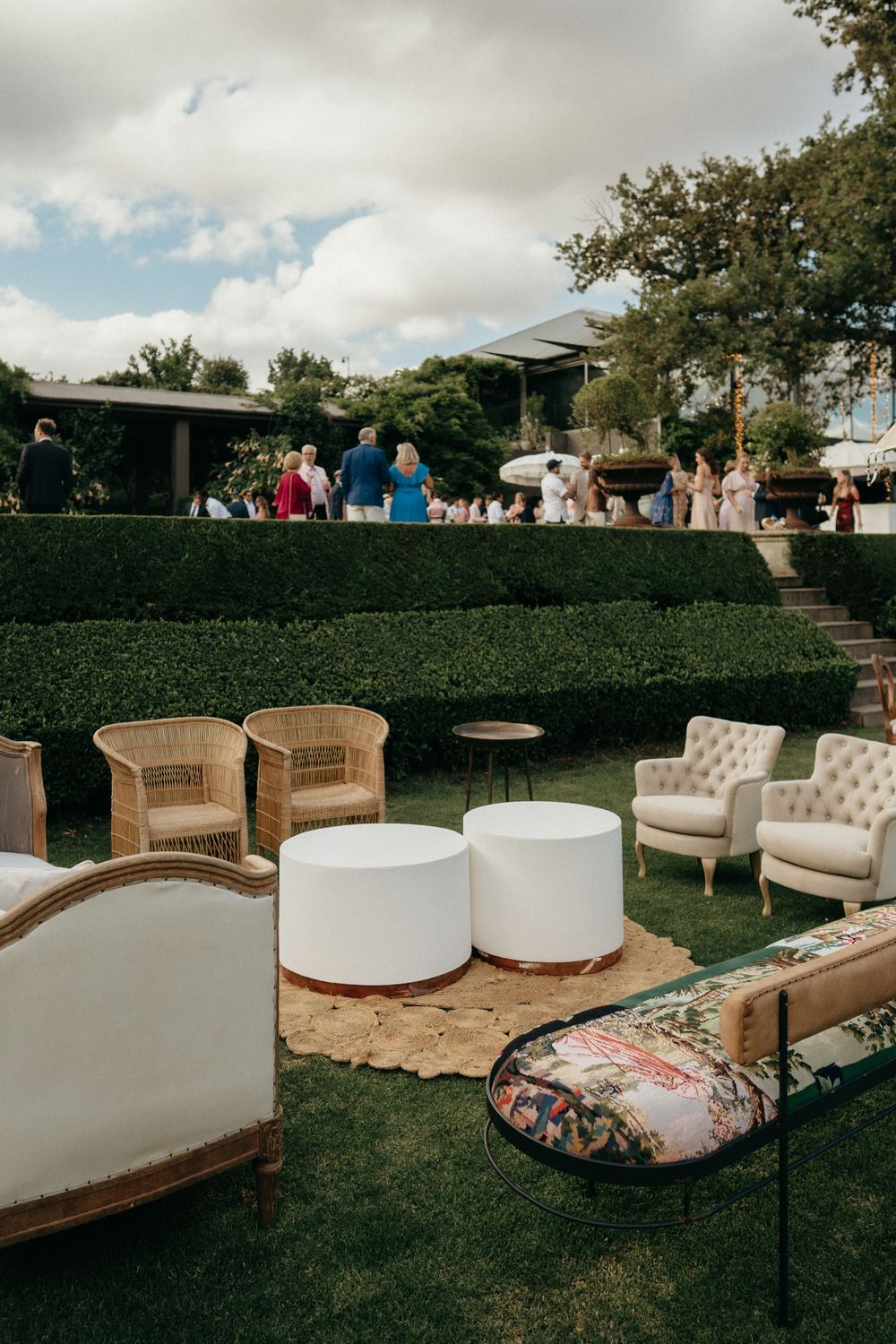 Elegant outdoor wedding lounge area with vintage furniture and white poufs on manicured lawn.