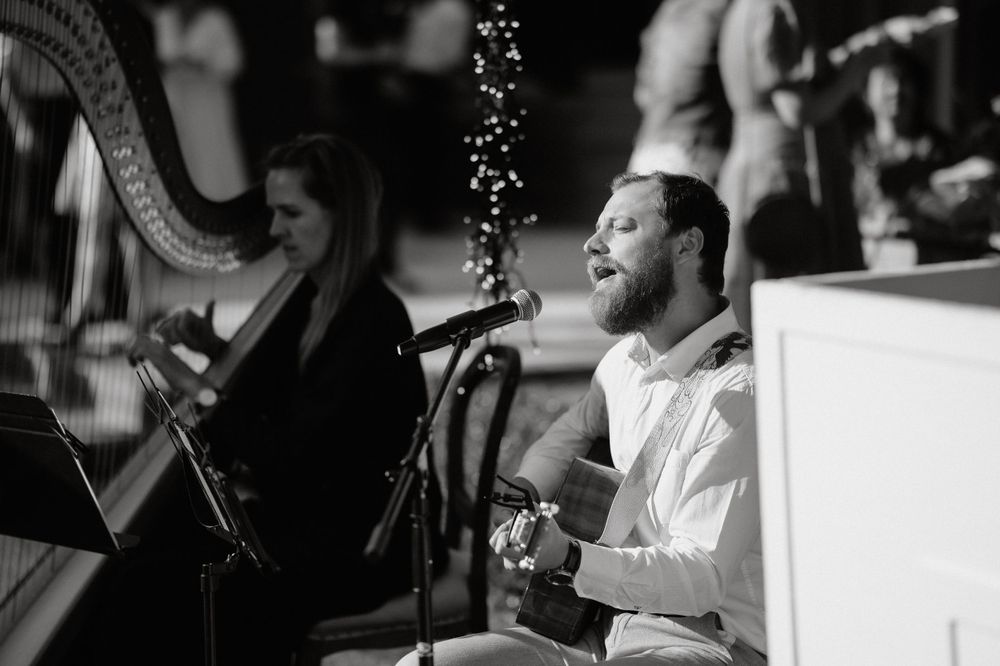 Musicians perform with harp and guitar during elegant evening wedding reception.
