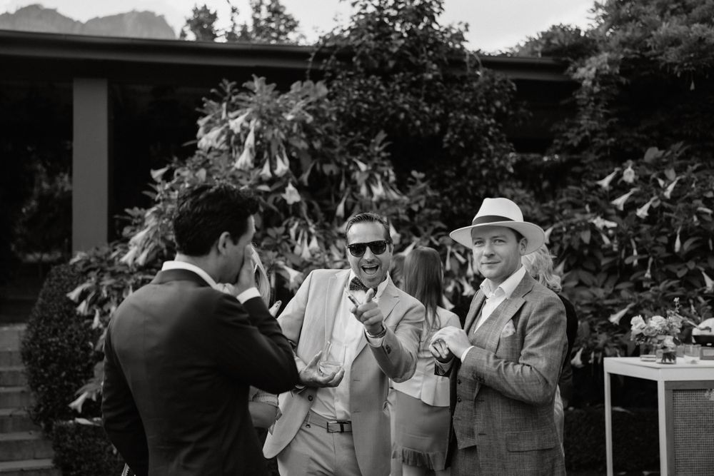 Black and white photo of wedding guests socializing in garden setting.