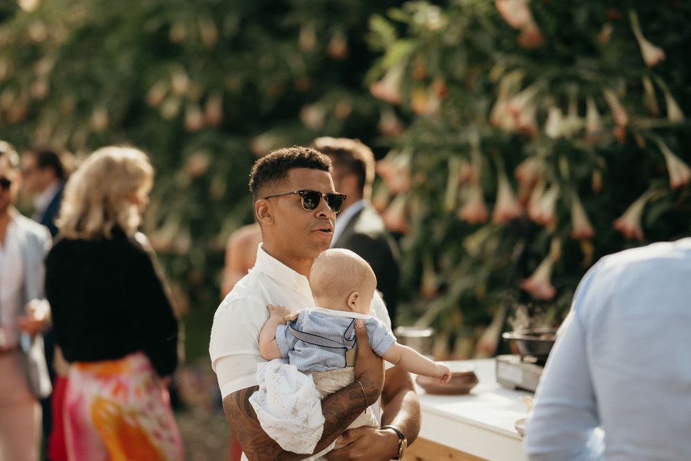 Guest in sunglasses holding an infant at an outdoor wedding reception.