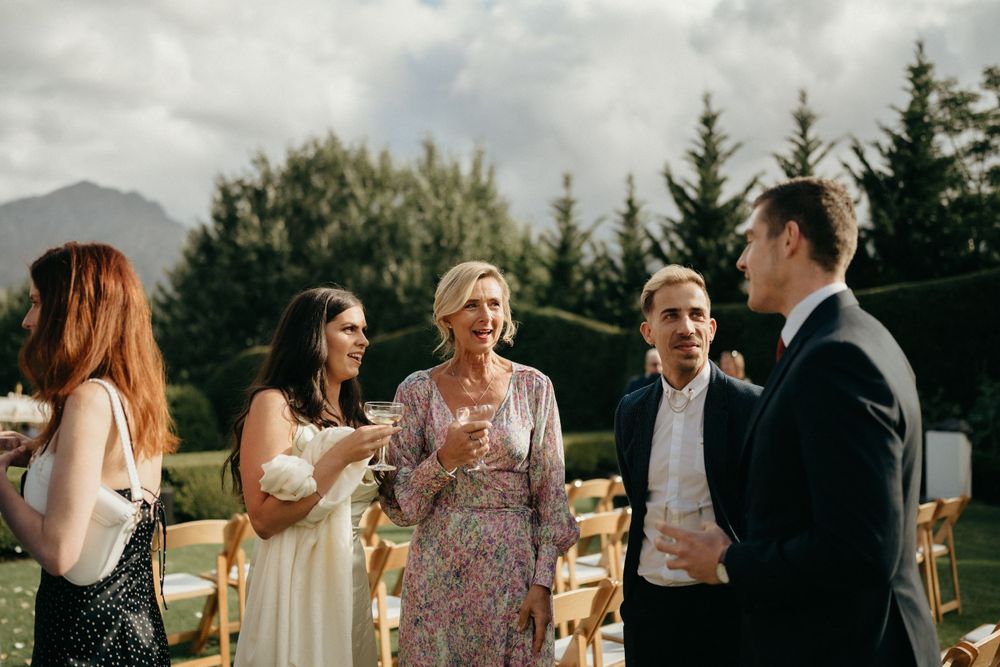 Outdoor wedding guests chatting with mountain scenery and pine trees in background.