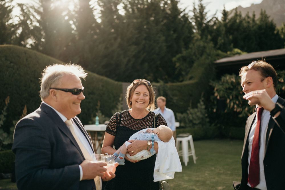 Wedding guests socialize and eat during an outdoor reception with mountains and trees in the background.