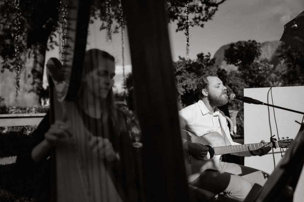 Black and white photo of musician performing with acoustic guitar in outdoor setting.