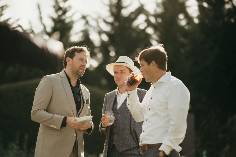 Three wedding guests in smart casual attire having drinks and conversation at sunset.