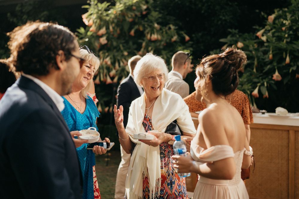Wedding guests mingle and socialize during an outdoor reception in warm sunlight.