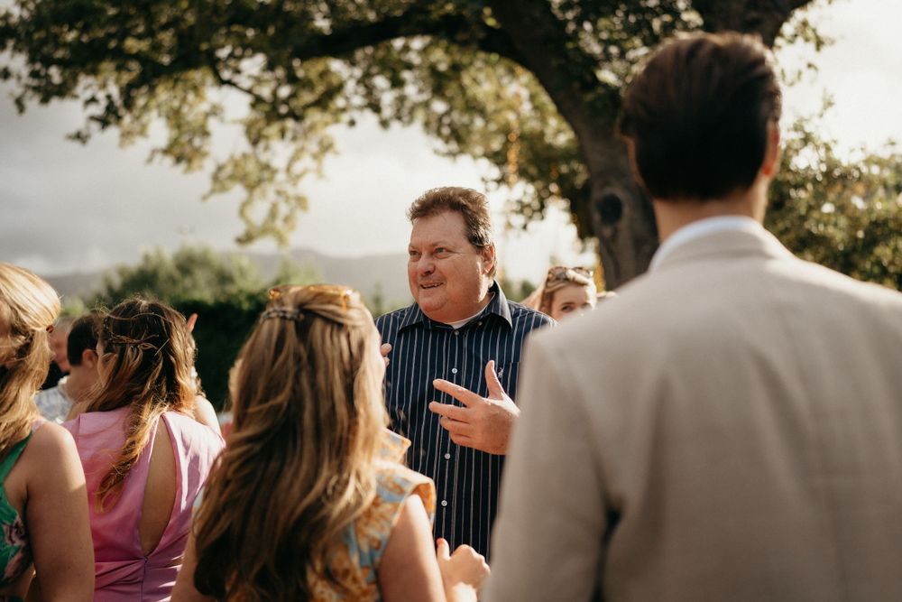 Group gathers outdoors under tree branches during a sunny afternoon social event.