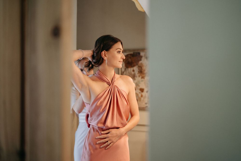 Person wearing coral-colored dress adjusting hair in soft indoor lighting.
