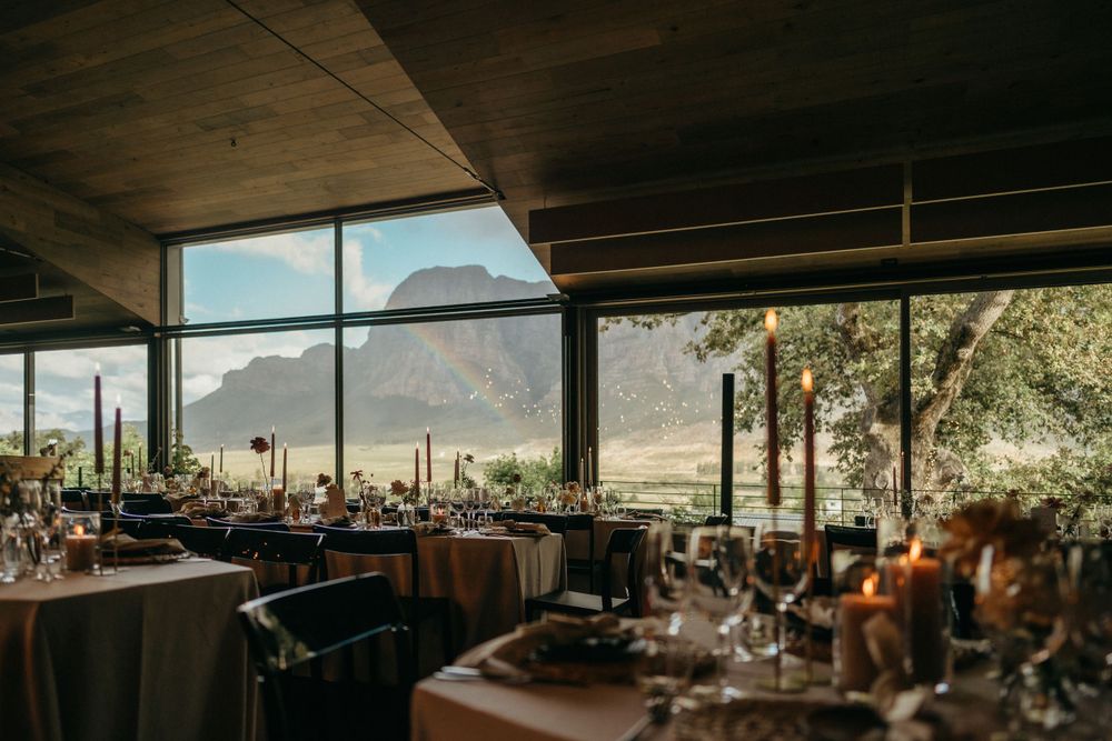 An elegant wedding reception venue with mountain views through large windows and set dining tables.