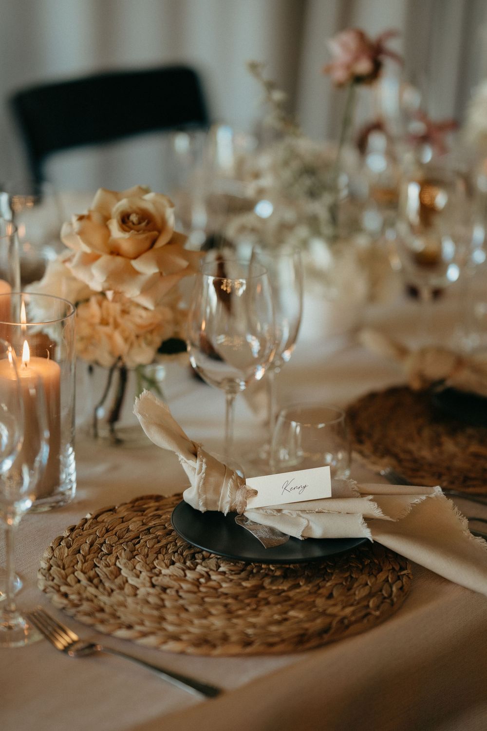 Elegant wedding table setting with peach roses, candles and woven placemats.