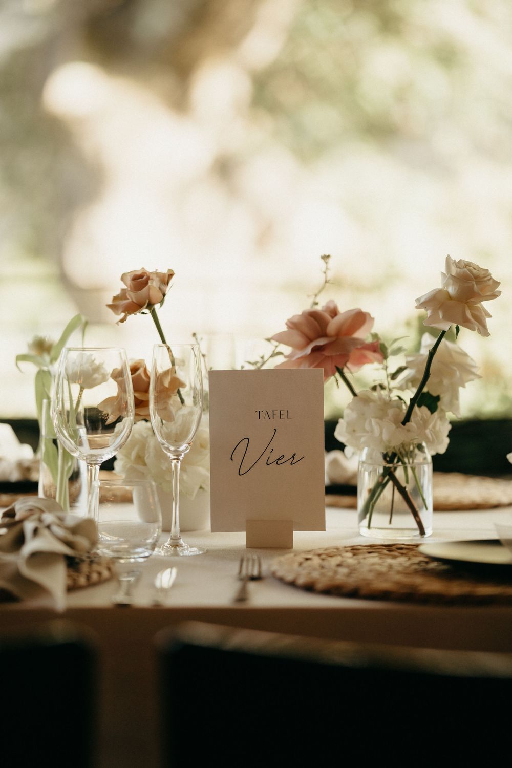 Rustic wedding table setting with delicate floral arrangements and glassware beside a table number card.
