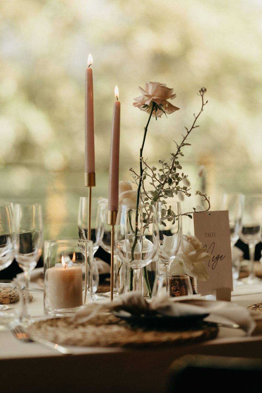 Elegant wedding table setting with tall candles, delicate flowers, and wine glasses in warm romantic lighting.
