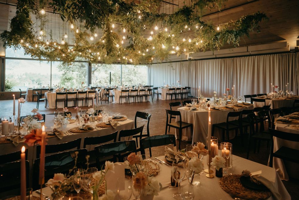 Modern wedding reception venue with string lights, greenery and round tables set for dining.