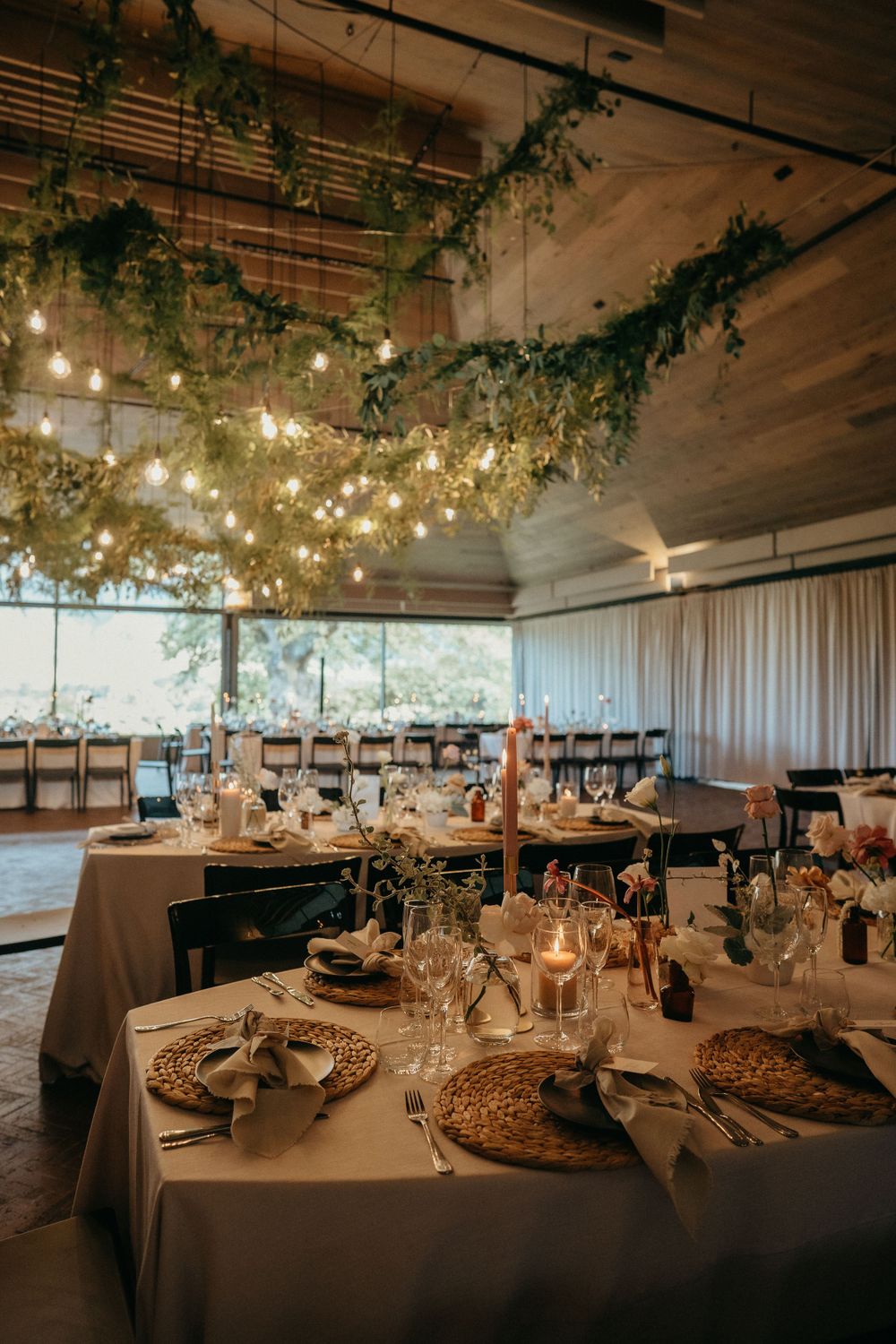 Elegant wedding reception venue with hanging greenery, string lights and beautifully set tables with candles and decor.