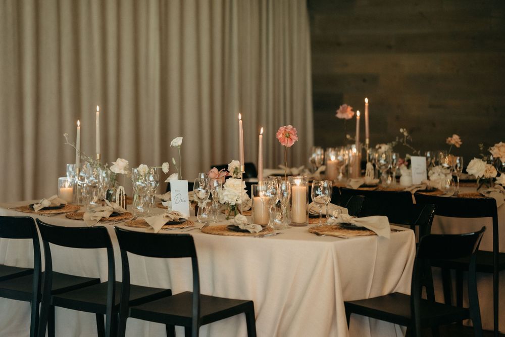 Elegant wedding reception table setting with white candles, linens, and romantic floral centerpieces.