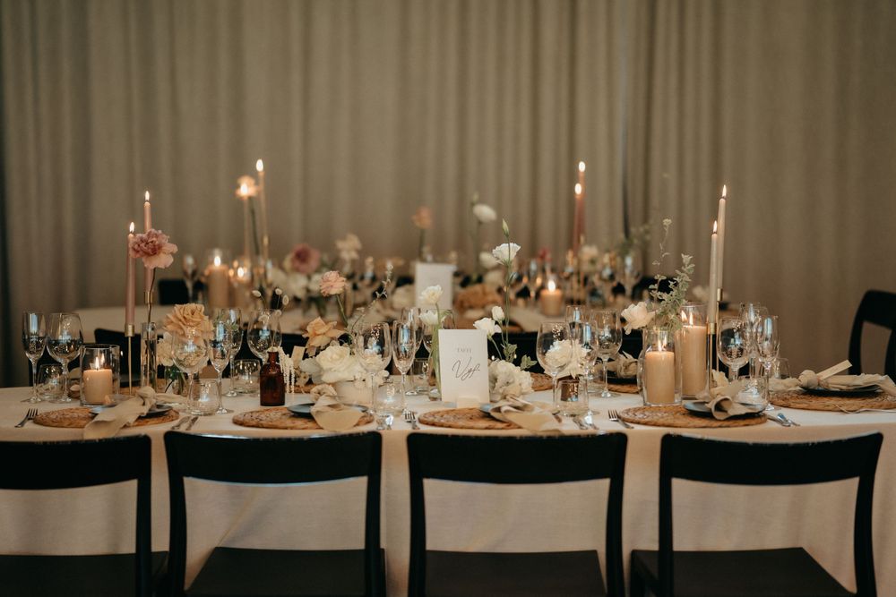 An elegant wedding reception table set with candles and minimal decor against neutral curtains.