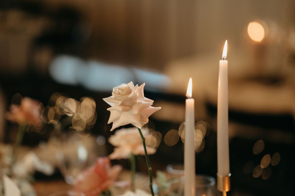 Close-up of white rose and lit taper candles creating romantic ambiance at wedding table setting.