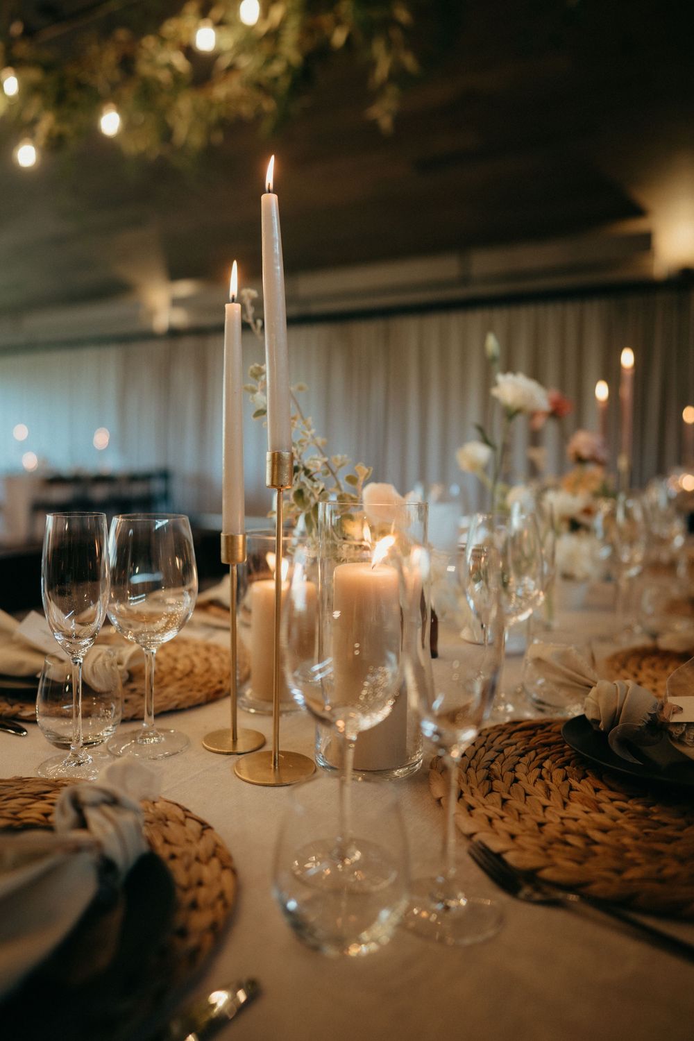 Elegant wedding table setting with tall candles, wine glasses, and woven placemats.