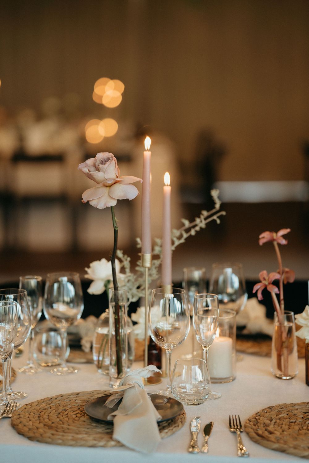 Elegant wedding table setting with white flowers, candles and wine glasses on woven placemats.