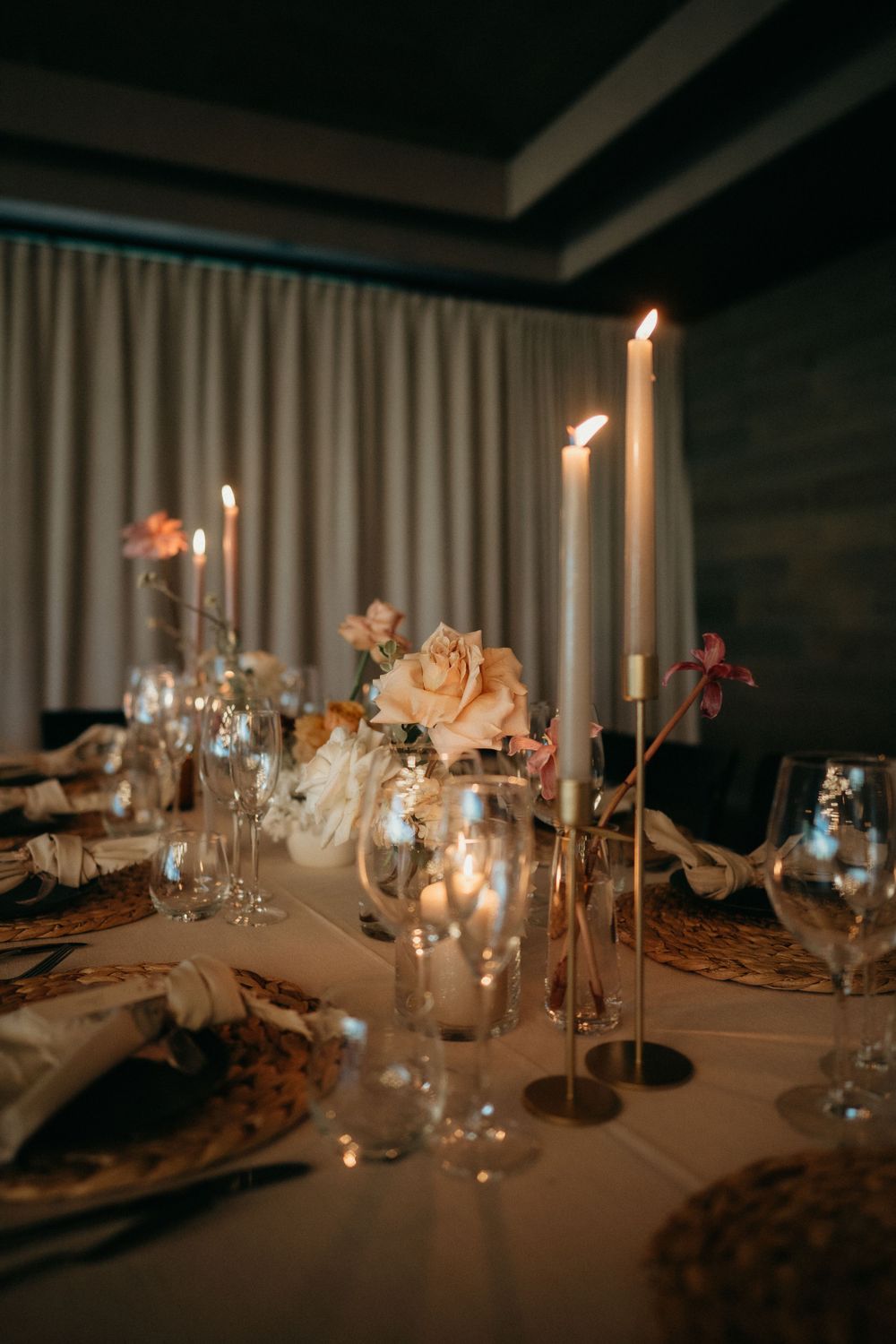 Elegant wedding table setting with tall candles, rose centerpieces, and ambient lighting creates romantic atmosphere.